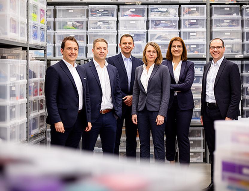 Geschäftsleitung von Uster Produkte in Zürich vor Lagerregalen mit Kunststoffboxen