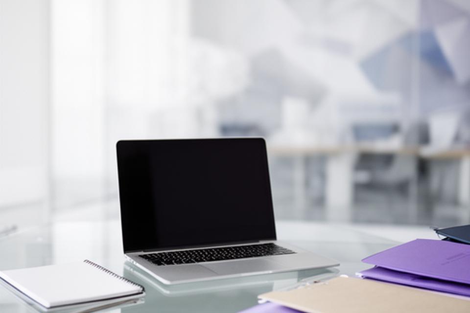Helle Büroaufnahme mit Laptop, Notizblock und geordneten Akten auf einem gläsernen Tisch